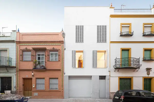 Fachada edificio con ladrillo visto y detalles de azulejos, junto a una moderna construcción blanca y otra amarilla con balcones de forja.