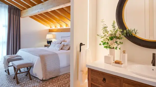 Habitación con vigas de madera y baño con espejo redondo. ¿Cuanto mide una habitación normal? Esta parece espaciosa.
