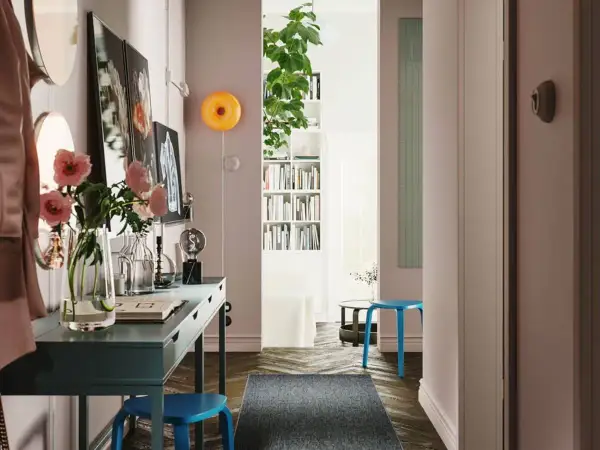 Un recibidor con pasillos con encanto: un escritorio azul, flores rosas, libros y un taburete.