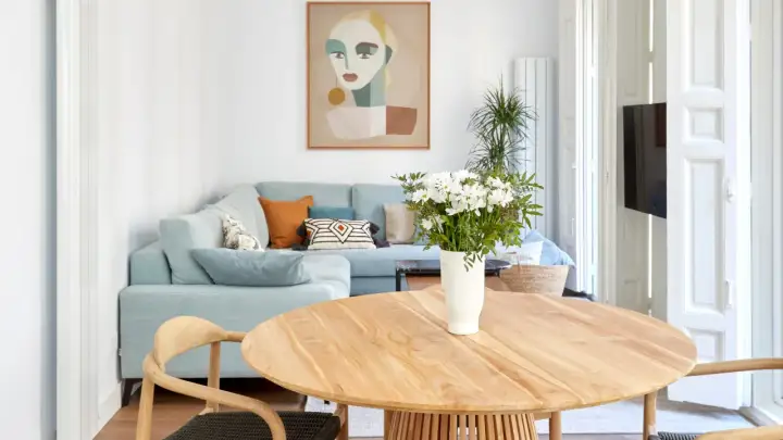 Elegante decoracion salon comedor con sofá azul claro, mesa de madera y cuadro abstracto.